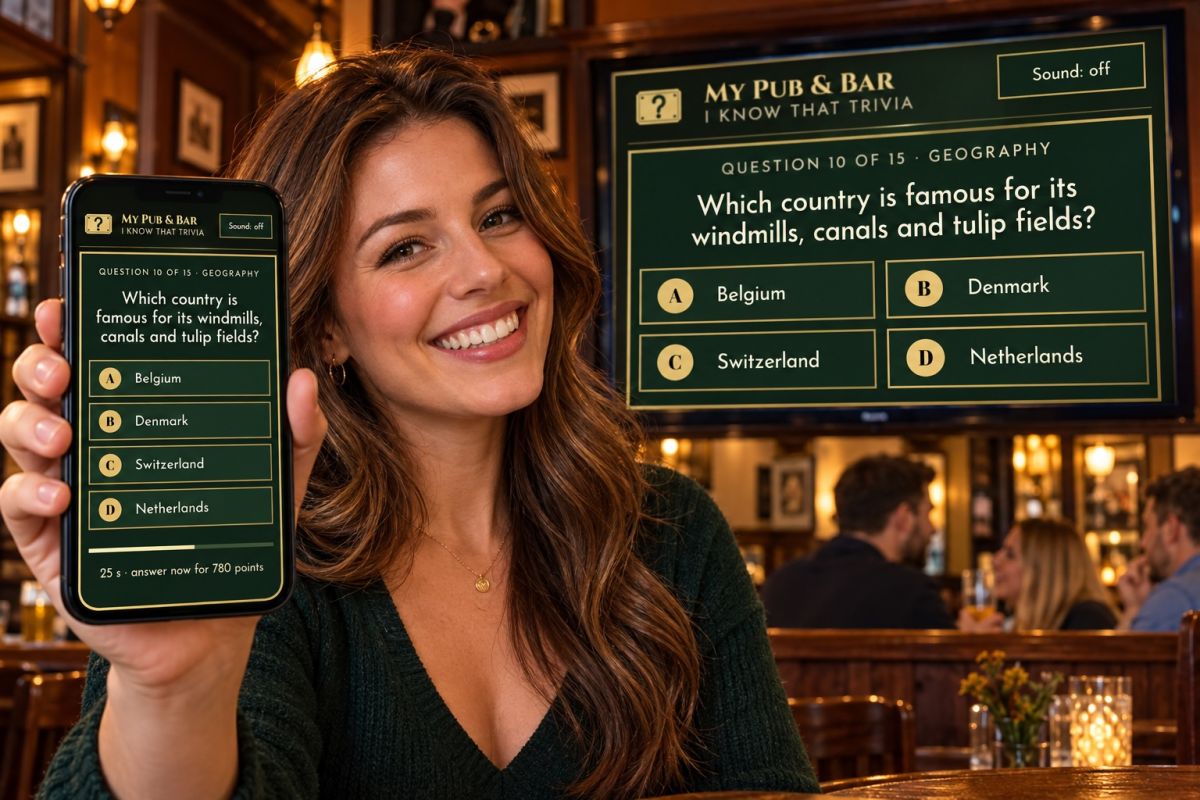 A smiling woman in a pub holds up her phone showing a geography question, with the same question on the big TV behind her.